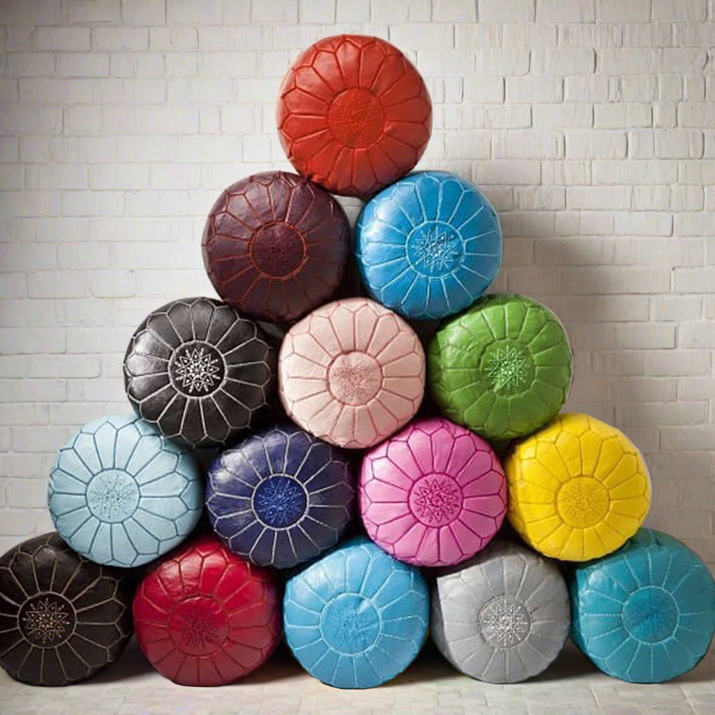 Colorful Moroccan leather poufs , stacked in a pyramid against a brick wall, showcasing a variety of vibrant colors and intricate handcrafted stitching by skilled women artisans.