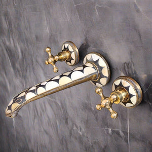 Wall-mounted faucet featuring a black and white geometric pattern and gold handles, installed on a gray tiled wall.