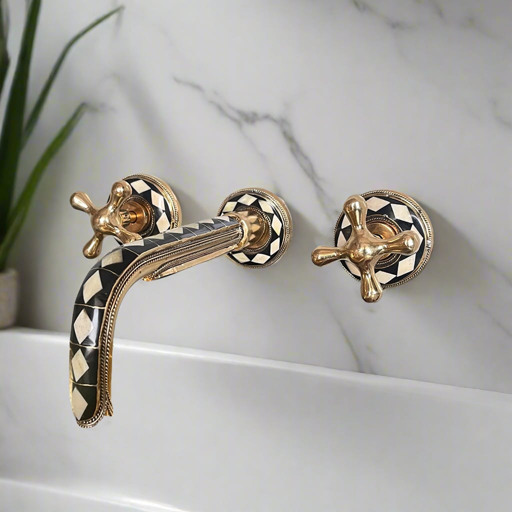Decorative wall-mounted inlay bathroom faucet with knob handles and black-and-brass geometric detailing over a marble wall