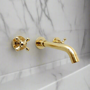 Side angle of a wall-mounted brass faucet with cross handles, installed over a marble basin