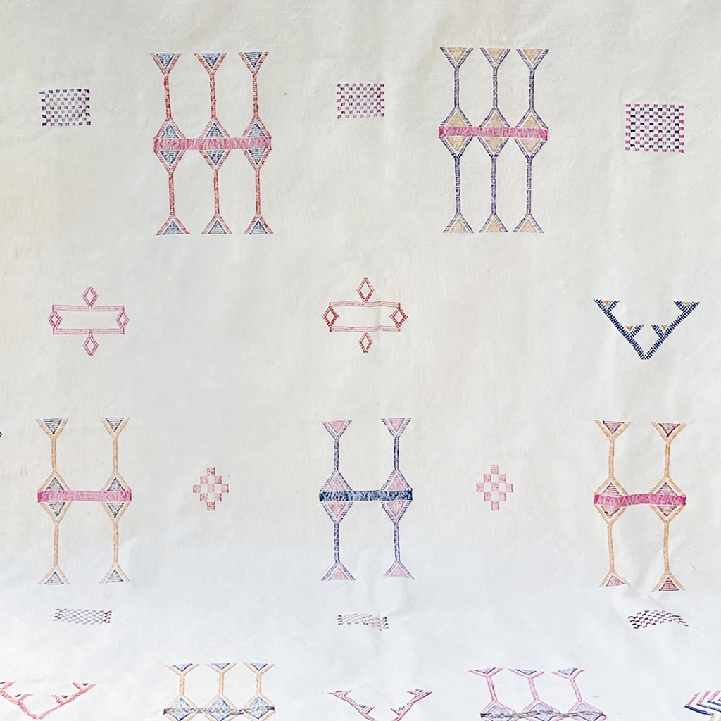 Close-up of a white Moroccan sabra cactus silk rug featuring intricate hand-embroidered Berber motifs in pink, blue, yellow, and purple