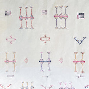 Close-up of a white Moroccan sabra cactus silk rug featuring intricate hand-embroidered Berber motifs in pink, blue, yellow, and purple