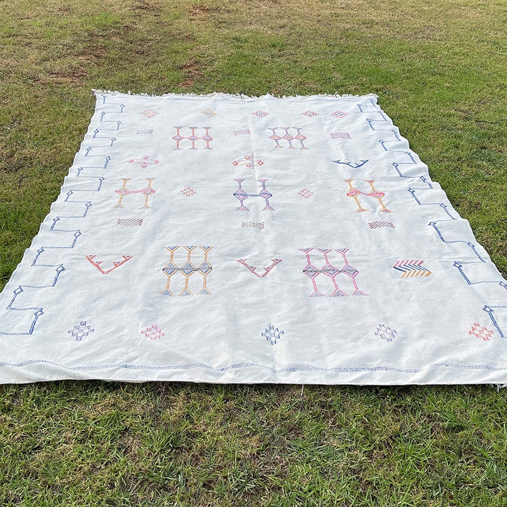 White Moroccan sabra cactus silk rug with geometric Berber embroidery and colorful tribal patterns, laid flat on grass
