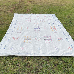 White Moroccan sabra cactus silk rug with geometric Berber embroidery and colorful tribal patterns, laid flat on grass