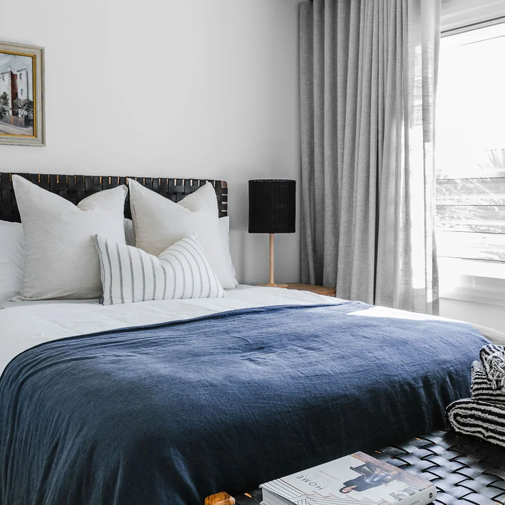 A bedroom with big window, bedside lamp, comfortable bed, white & blue bedclothes, white pillows, black leather headboard - Moroccan Interior
