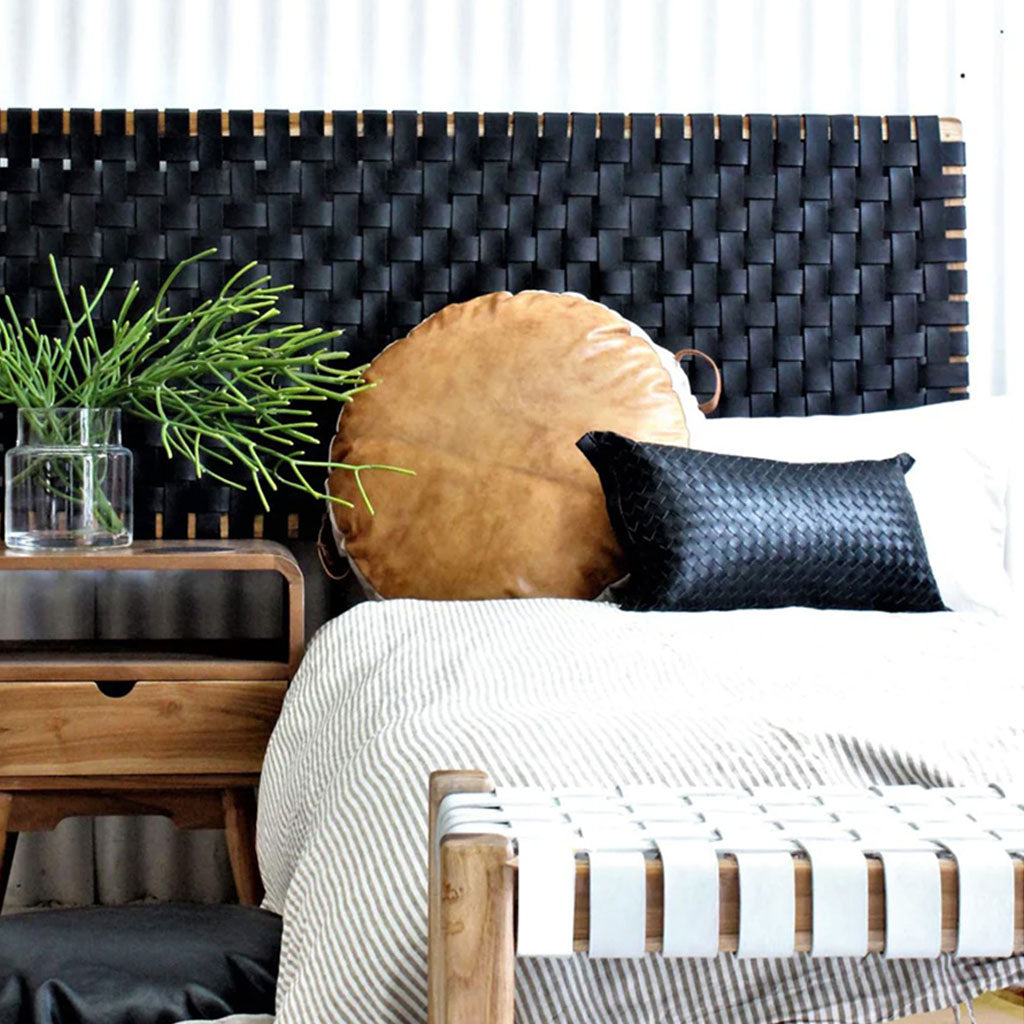 Striped blanket, round leather pillow, lumbar on bed with black leather headboard, wood bench, side table, flowers - Moroccan Interior