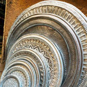 Moroccan aluminum trays of various sizes in front of an aged wall at a small shop in Marrakesh - Moroccan Interior.