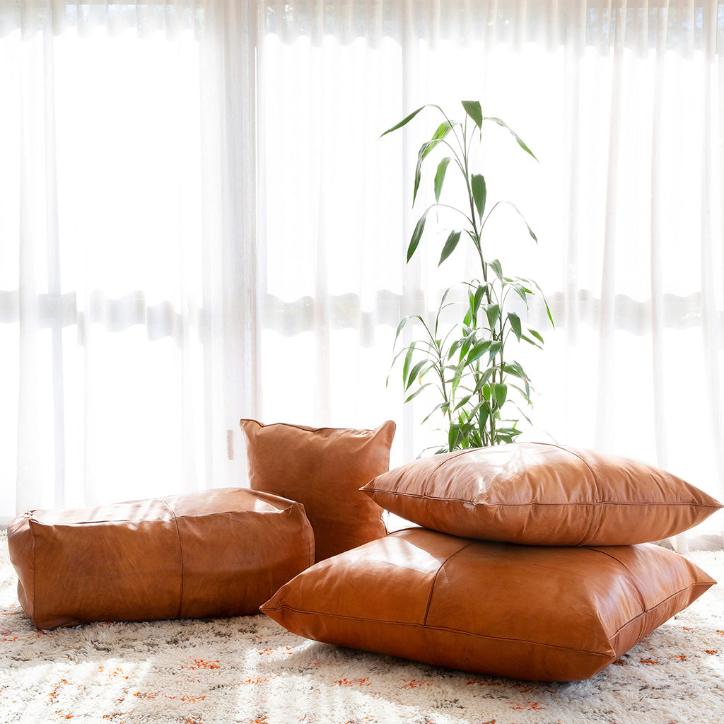 Moroccan leather pillows over a wool rug in a living room with big window and a big plant - Moroccan Interior