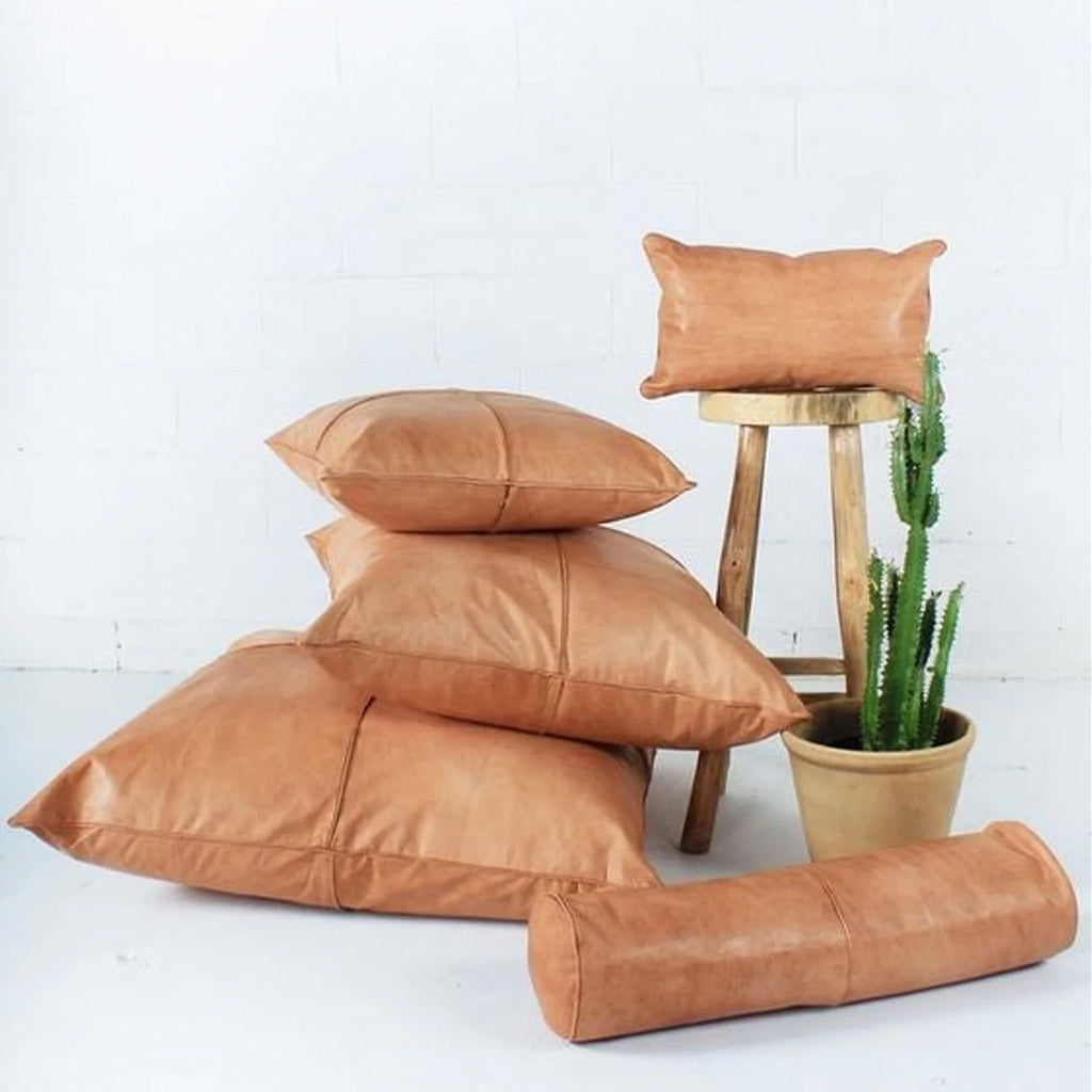 Moroccan Leather Pillows in different sizes on the floor of a room close to a cactus plant and a wood stool  - Moroccan Interior