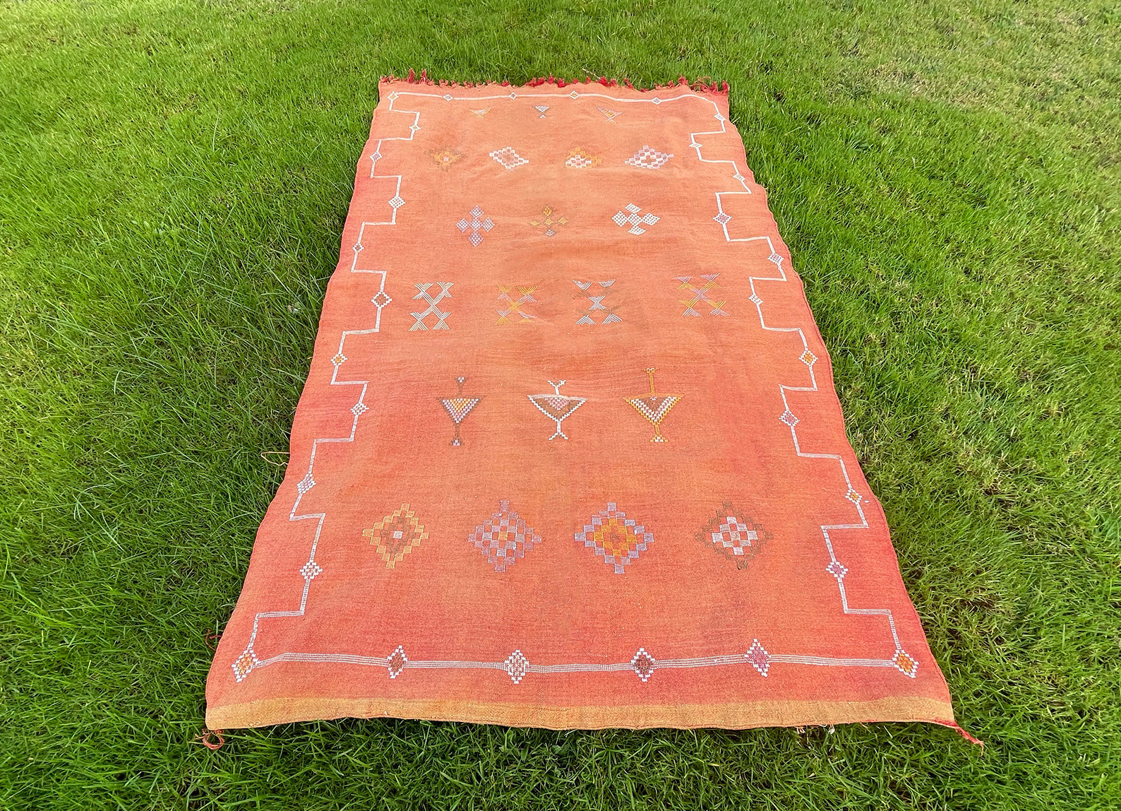 Moroccan Sabra rug laid flat, revealing traditional Berber symbols and soft earth-tone hues on a pale orange background. Made from natural cactus silk, perfect for living room or bedroom décor