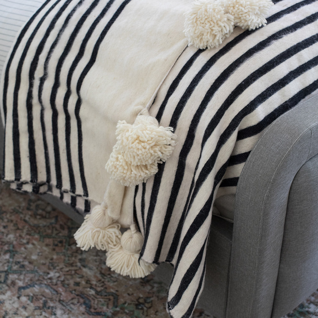 White and black Moroccan Pom pom blanket on top of a bed with pillows in a bedroom - Moroccan Interior