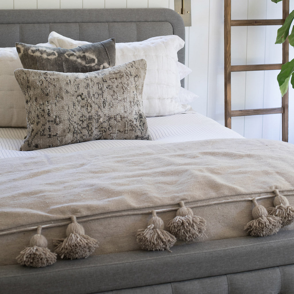 Beige Moroccan Pom pom blanket on top of a bed with pillows in a bedroom with furniture - Moroccan Interior