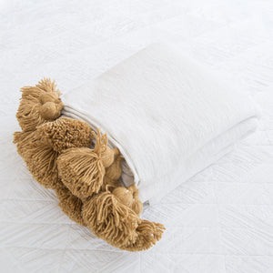 Folded Moroccan cotton blanket with beige pom poms on a clean white surface