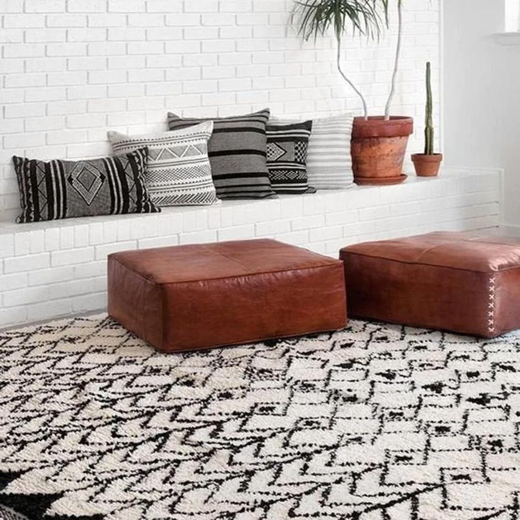 Moroccan Square Leather Pouf on wool rug by white wall, adorned with gray-black pillows - Moroccan Interior